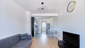 Un salon moderne avec un canapé gris, un téléviseur à écran plat et un coin repas comprenant une table et des chaises.