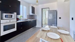 Une cuisine moderne avec des appareils électroménagers noirs et blancs, une table à manger en bois mise avec des assiettes et des couverts, et un sol à motifs.