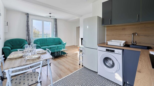 A compact living space with a dining area, a sofa, a washing machine, and a kitchenette. - Appartement Évasion Normande - Welkeys (Cabourg)