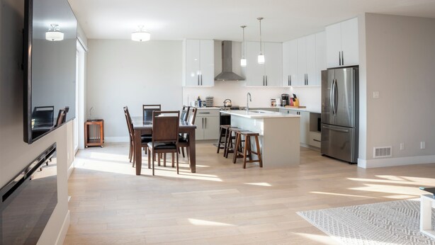 Een moderne keuken met witte kastjes, een roestvrijstalen koelkast, en een eethoek met houten stoelen en een tafel.
