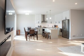 Une cuisine moderne avec des meubles blancs, un réfrigérateur en acier inoxydable et un coin repas comprenant des chaises et une table en bois.