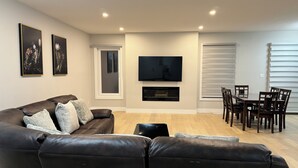 Een woonkamer met een leren bank, een flatscreen televisie, een eettafel met stoelen en een open haard.