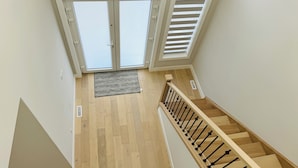 Uitzicht op een houten trap met een leuning, leidend naar een plateau met een deur en een raam met luiken.