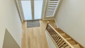 A view from a second-floor window overlooking a wooden staircase with a black railing, a door with glass panels, and a skylight with horizontal blinds. - Luxury with comfort  (Komoka)