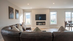 A modern living room with a leather sofa, a flat-screen TV, and large windows offering a view of the outdoors. - Luxury with comfort  (Komoka)