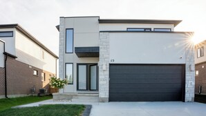 A modern two-story house with a garage, a well-maintained lawn, and a small flower bed. - Luxury with comfort  (Komoka)