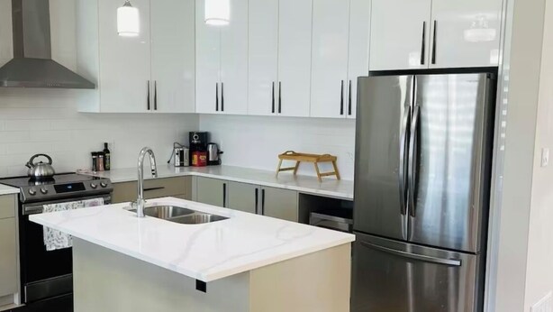 A modern kitchen with white cabinets, stainless steel appliances, and a central island with a sink. - Luxury with comfort  (Komoka)