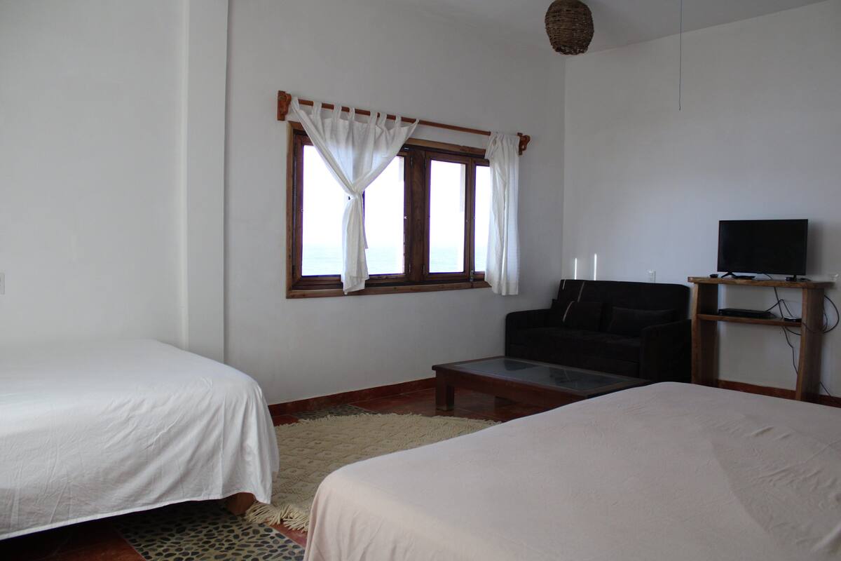A room with two beds, a sofa, a television, and a window with curtains.