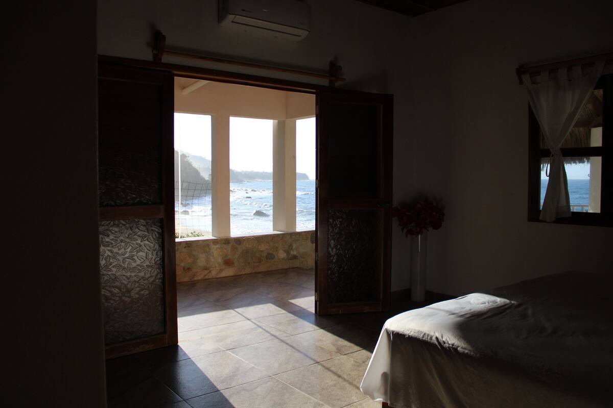 A bedroom with a bed, a window with curtains, and a view of the sea.