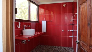 A bathroom with red tiled walls, a white sink, a towel rack, and a shower with a white door.