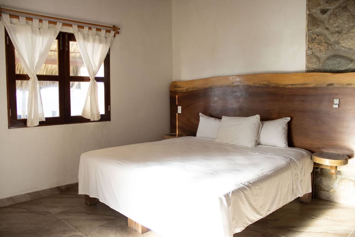 A bedroom with a large bed, wooden headboard, a window with curtains, and a stone wall.