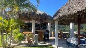 A tropical outdoor area with thatched-roof structures, a dining table, and a bed.