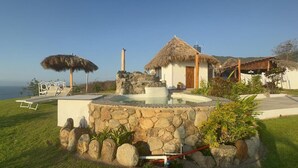 A stone fountain, a thatched-roof structure, and a white building with a wooden door.