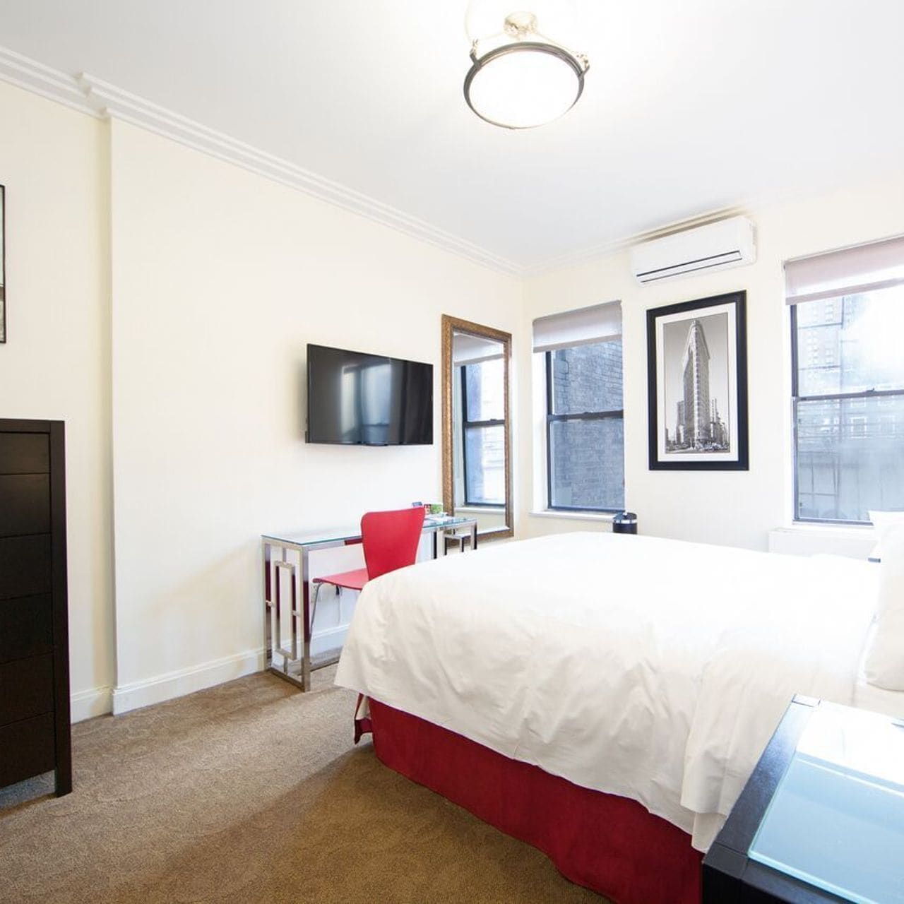 A hotel room with a large bed, a desk with a chair, a TV, and a window with a cityscape view.