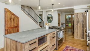 A kitchen with a central island, wooden cabinets, a stove, and a microwave. There is a staircase with a wooden door and a hanging light fixture. - Lincoln Lodge! Steps from the heart of Elk Avenue! (Crested Butte)