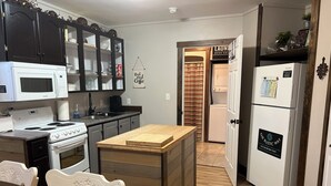 Cozinha equipada com micro-ondas, fogão, pia e frigorífico. Possui uma ilha de madeira com tábua de corte.