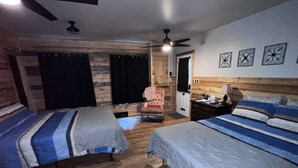Quarto com duas camas, piso de madeira, ventoinha no teto e porta que dá para outro espaço.
