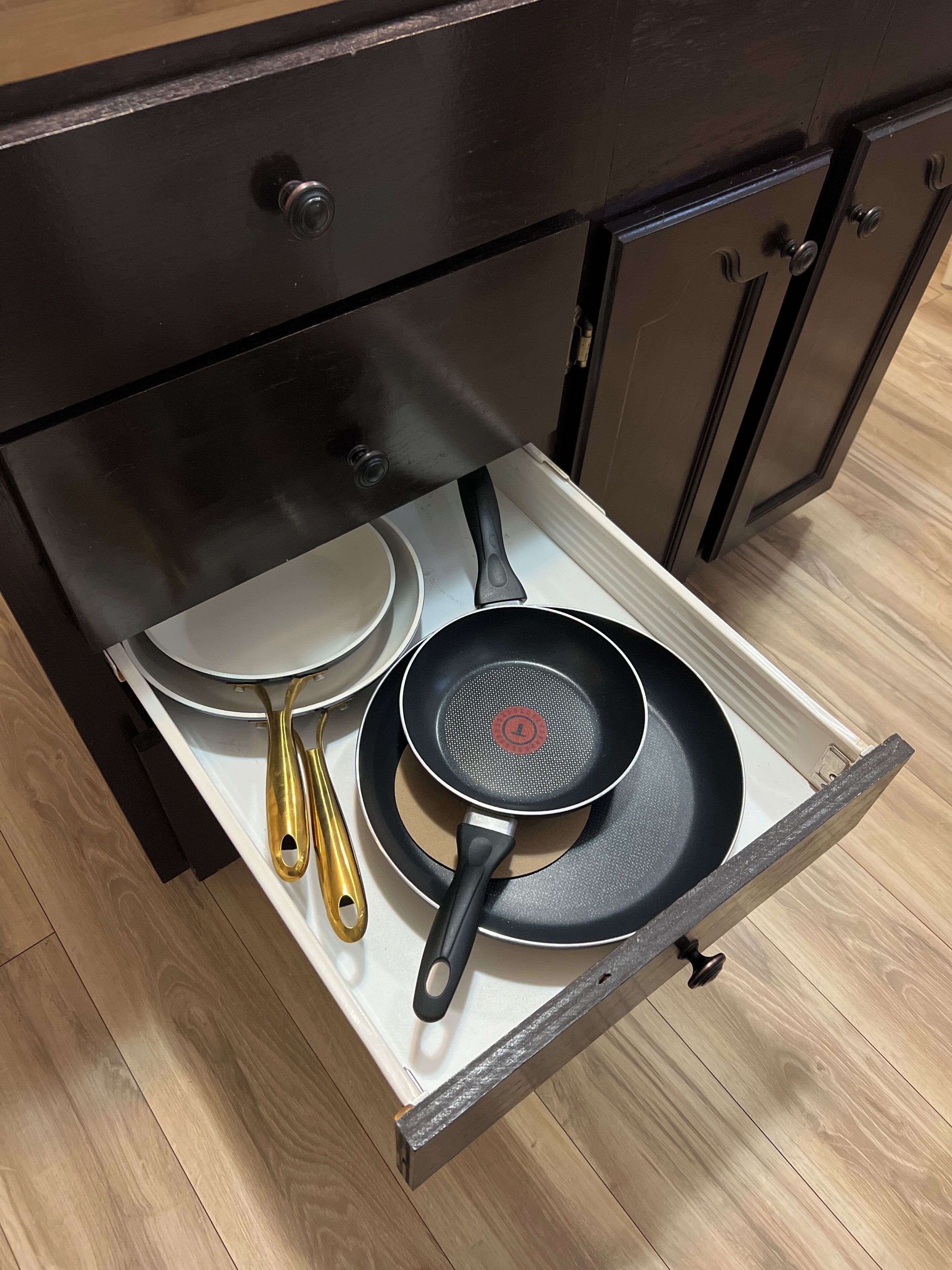 A kitchen drawer with a frying pan, a spatula, and a pan lid.
