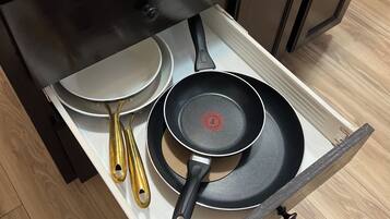 A kitchen drawer with a frying pan, a spatula, and a pan lid.
