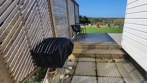 A patio with a grill, a table, and chairs, leading to a grassy yard.
