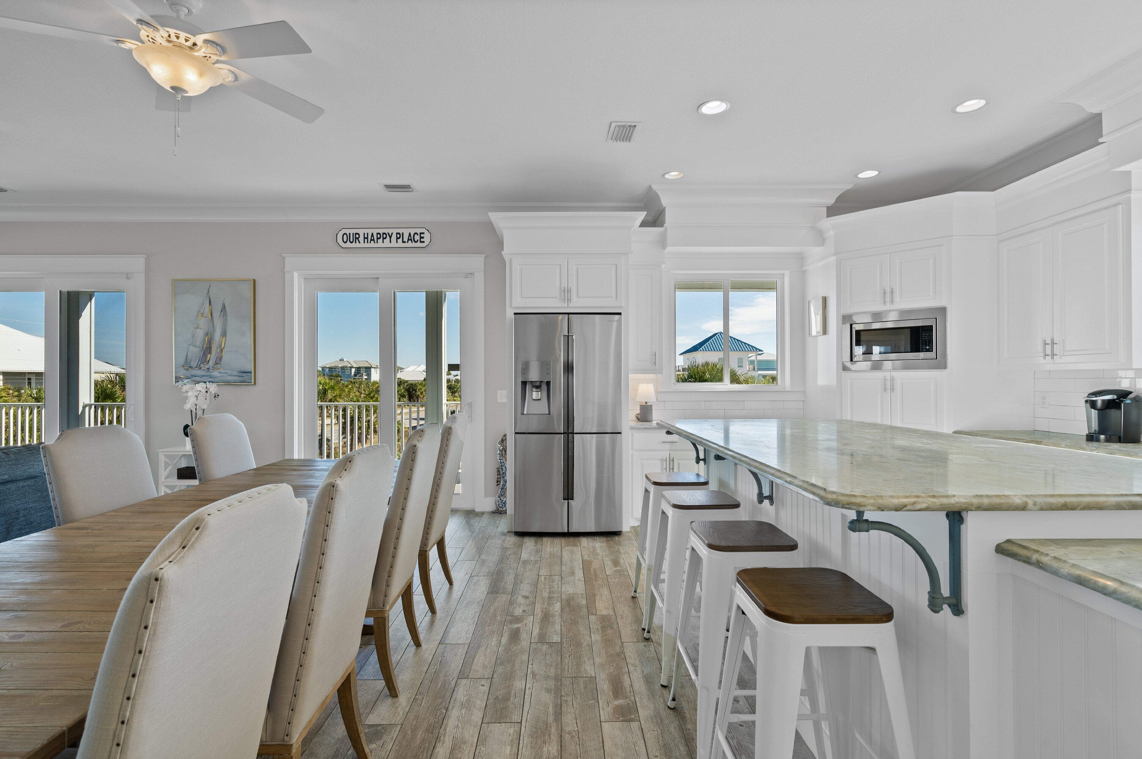 A modern kitchen with white cabinetry, a stainless steel refrigerator, and a large island with bar stools.