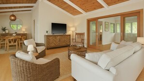 Ein geräumiges Wohnzimmer mit Holzboden, einem Fernseher, einem Essbereich mit Tisch und Stühlen sowie einem großen Sofa.