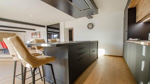 Une cuisine moderne avec un îlot central, des tabourets de bar et une horloge au mur.