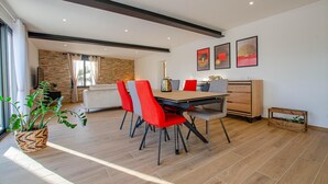 Un coin repas avec une table en bois, des chaises rouges et grises, et une cuisine moderne en arrière-plan.