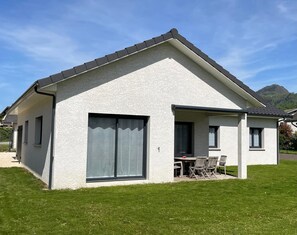 Una casa a un piano con un'ampia porta scorrevole in vetro, un patio con mobili da esterno e una montagna sullo sfondo.
