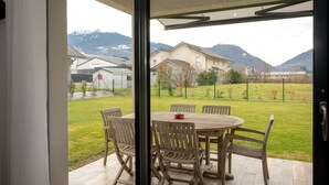 An open patio with a round wooden table and chairs, a view of a residential area with houses and mountains in the background. - Holiday Home 'Les Chaudannes' with Mountain View, Wi-Fi, and Air Conditioning (Valgelon-La Rochette)
