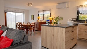 A modern kitchen with wooden cabinets, a dining area with a table and chairs, and a sofa with red cushions. - Holiday Home 'Les Chaudannes' with Mountain View, Wi-Fi, and Air Conditioning (Valgelon-La Rochette)