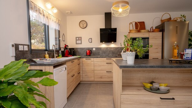 A modern kitchen with wooden cabinets, a built-in microwave, and a large window with curtains. - Holiday Home 'Les Chaudannes' with Mountain View, Wi-Fi, and Air Conditioning (Valgelon-La Rochette)