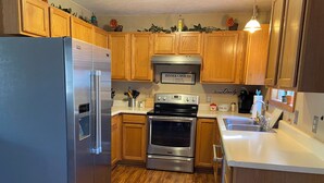 A kitchen with wooden cabinets, a stainless steel refrigerator, an oven, and a sink. - Charming 4-bedroom house in Interlochen. Your home away from home.  (Interlochen)