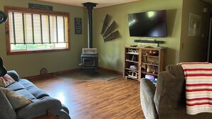 A cozy living room with a fireplace, a television, and a bookshelf. - Charming 4-bedroom house in Interlochen. Your home away from home.  (Interlochen)