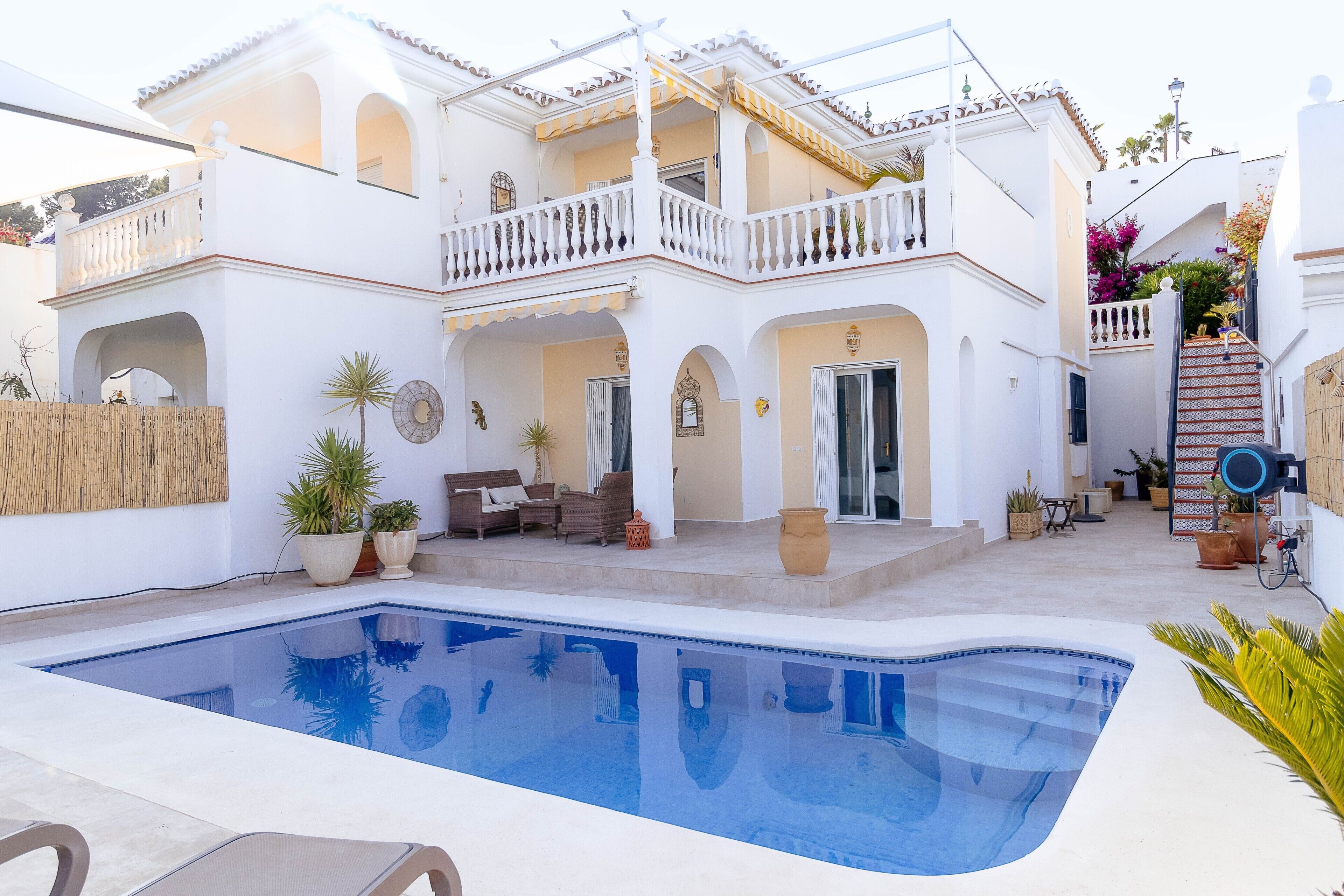 Una casa de dos pisos con piscina, mobiliario de exterior y plantas en macetas.