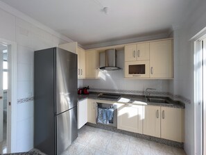 Uma cozinha compacta com geladeira de aço inoxidável, armários bege, forno embutido e bancada de granito.