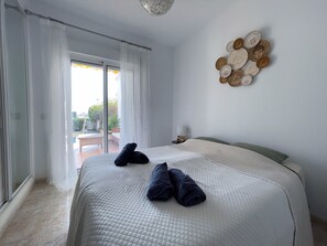 Quarto com cama, cortina, decoração na parede e vista pela janela.