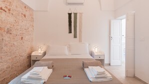 Une chambre d’hôtel avec un mur en briques, un lit avec deux oreillers, une table de chevet avec une lampe et une porte donnant sur une autre pièce.