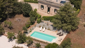 Vue aérienne d’une propriété dotée d’une piscine, de chaises longues et d’un bâtiment en pierre avec un balcon.