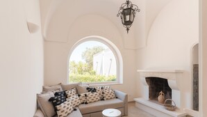 Un salon chaleureux avec un canapé, une table basse ronde, une cheminée et une grande fenêtre en arc de cercle.