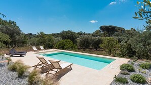 Une piscine rectangulaire à l’eau d’un bleu limpide, entourée d’une terrasse beige agrémentée de chaises longues.