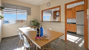 A dining area with a wooden table, chairs, a tray with food and drinks, a clock on the wall, and a view of the city through the window.