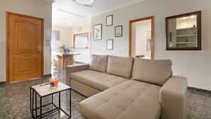 A living room with a sofa, a small table, a wooden door, and framed pictures on the wall.