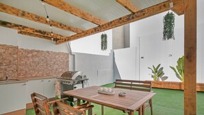 An outdoor patio with a wooden table and chairs, a grill, and hanging plants.
