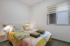 Una camera da letto con un letto, cuscini, una lampada da comodino, una finestra e una mensola a parete.