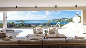 Una sala de estar moderna con un amplio ventanal que da a un balcón con vistas a la costa.