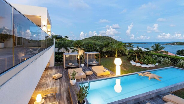 Un área de piscina moderna al aire libre con sillones de descanso y vistas al mar.