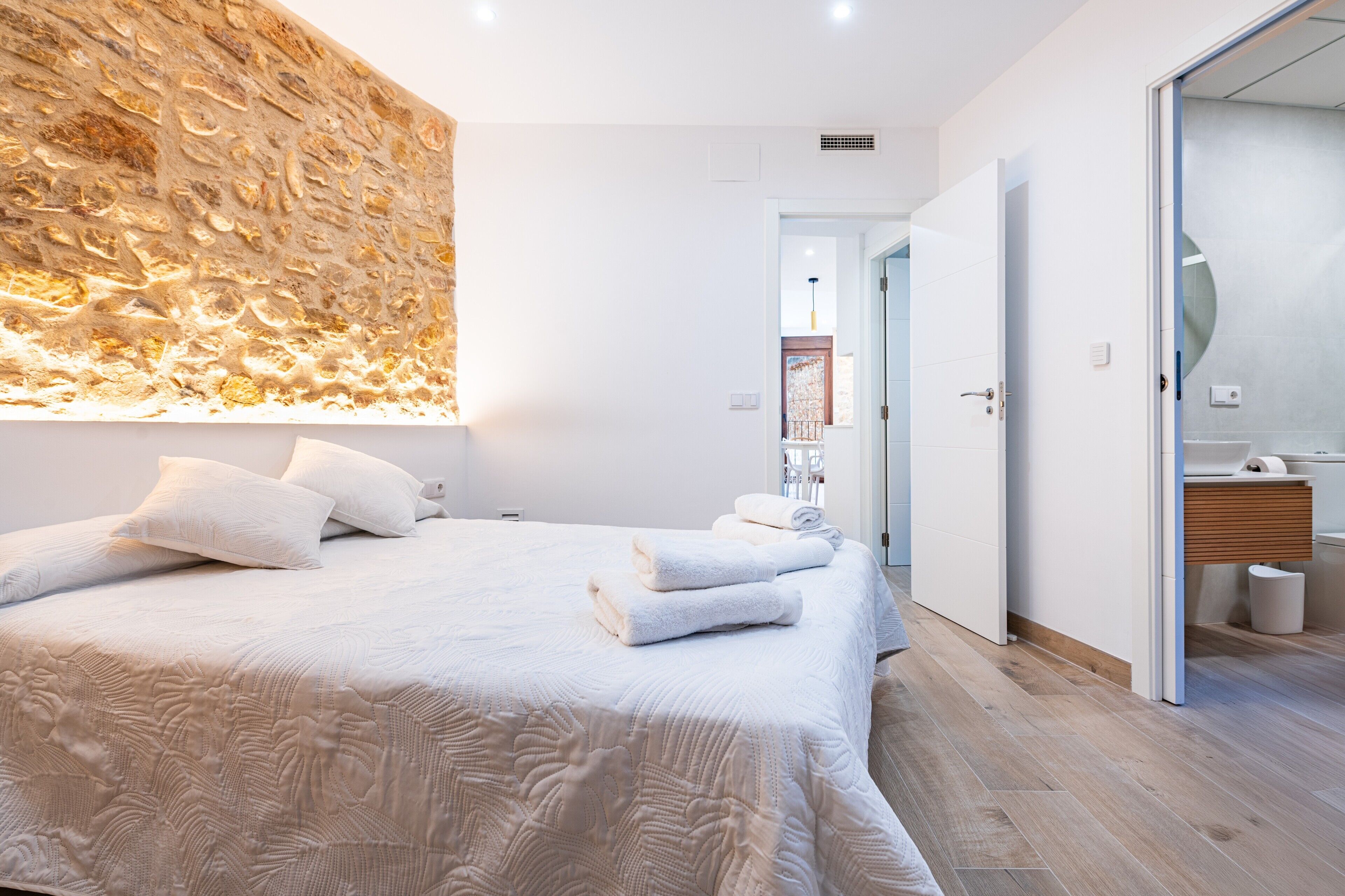 Un dormitorio moderno con una cama grande, una pared con textura y un baño con tocador de madera.