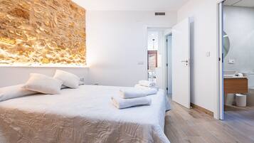Un dormitorio moderno con una cama grande, una pared con textura y un baño con tocador de madera.