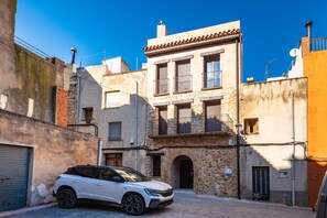 A white SUV parked in a narrow street with stone buildings, a visible door, and a small potted plant.